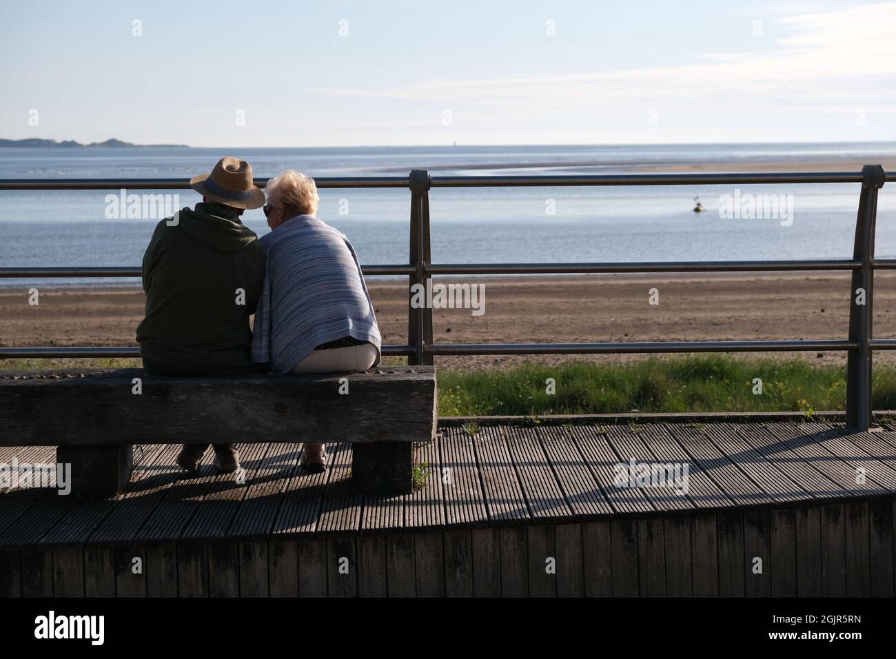 Un paio di età pensionabile seduti su una panchina su misura che si affaccia sulla spiaggia di llanelli e la penisola di Gower in lontananza Foto Stock
