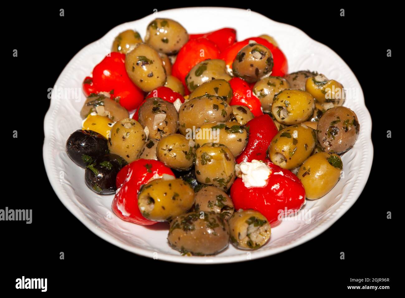 Olive sott'aceto con peperoni ripieni in un piatto bianco, isolate su sfondo nero Foto Stock