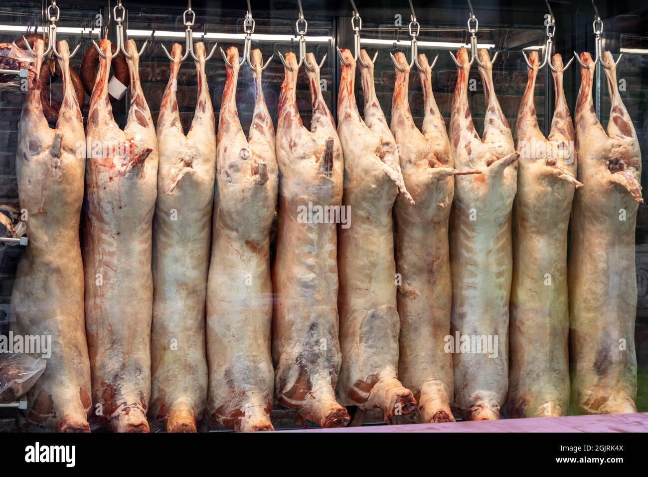 Carne di carcassa di agnello appesa ai ganci nel macello, macelleria negozio sono nel mobile frigorifero. Carne di agnello cruda non cotta Foto Stock