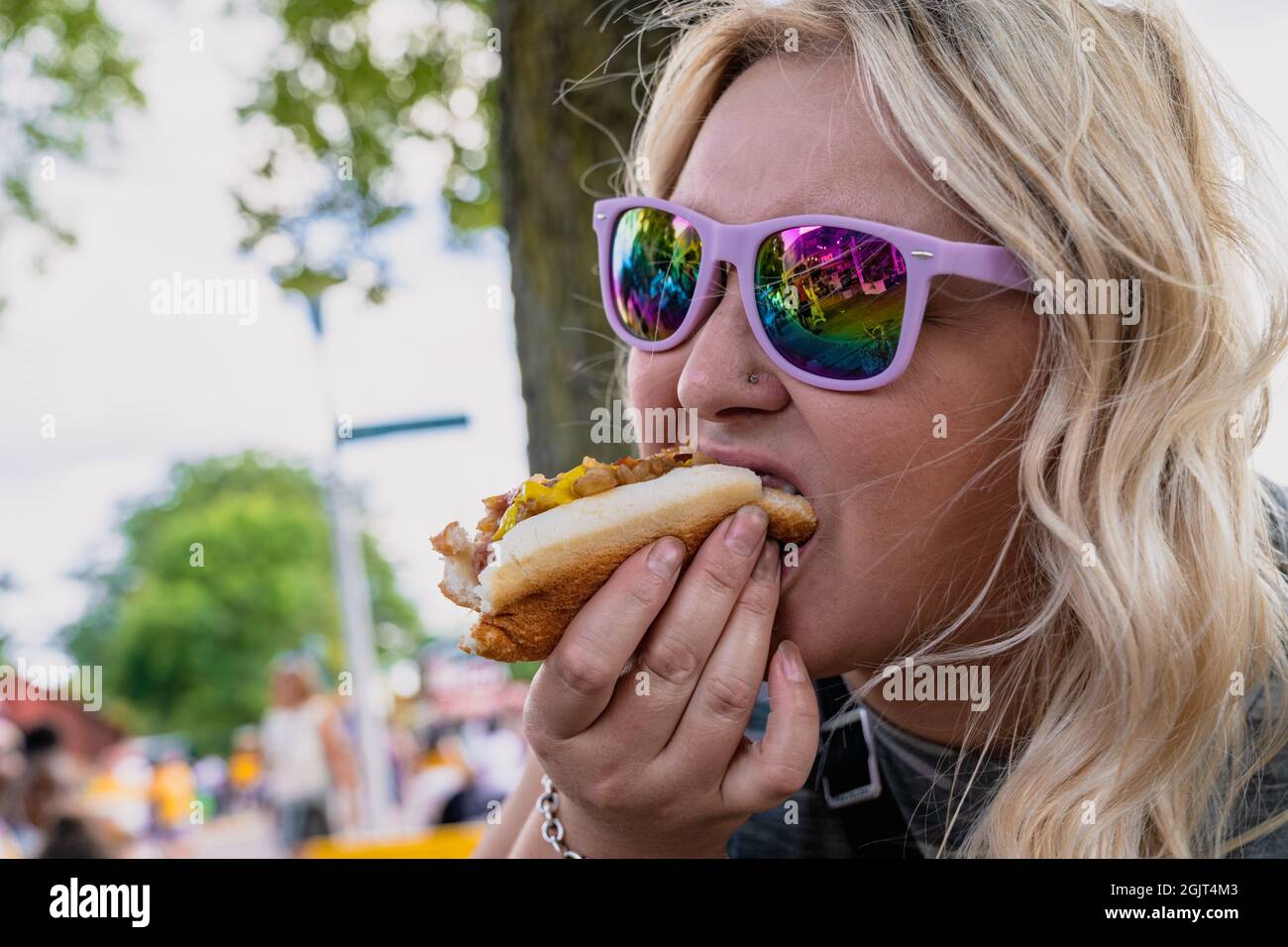 La donna bionda mangia e chows giù un hot dog a piedi alla fiera dello stato in Minnesota Foto Stock