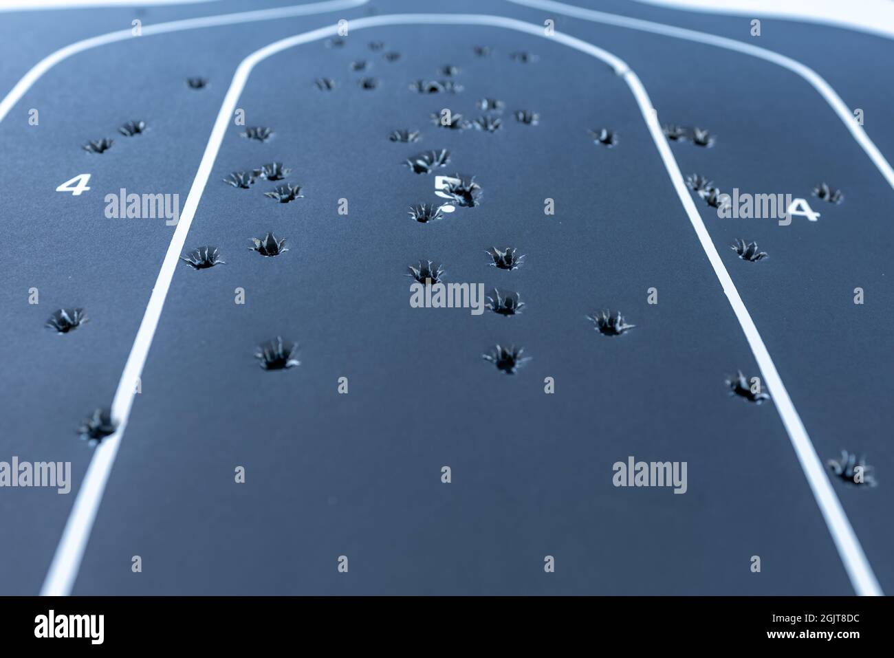 Primo piano con una profondità di campo poco profonda di un bersaglio di silhouette in carta nera con più fori di pallottola all'interno. Foto Stock