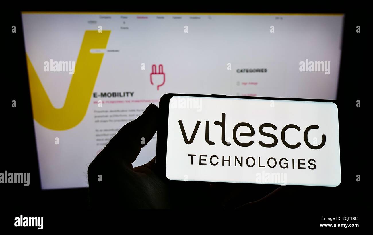 Persona che tiene uno smartphone con il logo del fornitore automobilistico tedesco Vitesco Technologies sullo schermo di fronte al sito web. Mettere a fuoco sul display del telefono. Foto Stock