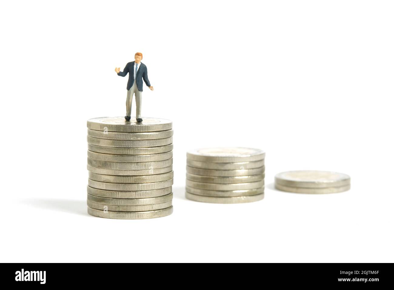 Fotografia di personaggi giocattolo in miniatura. Concetto di piano finanziario. Un uomo d'affari che si è arruggito si levano in piedi sopra la pila decrescente di soldi della moneta. Isolato su bianco ba Foto Stock