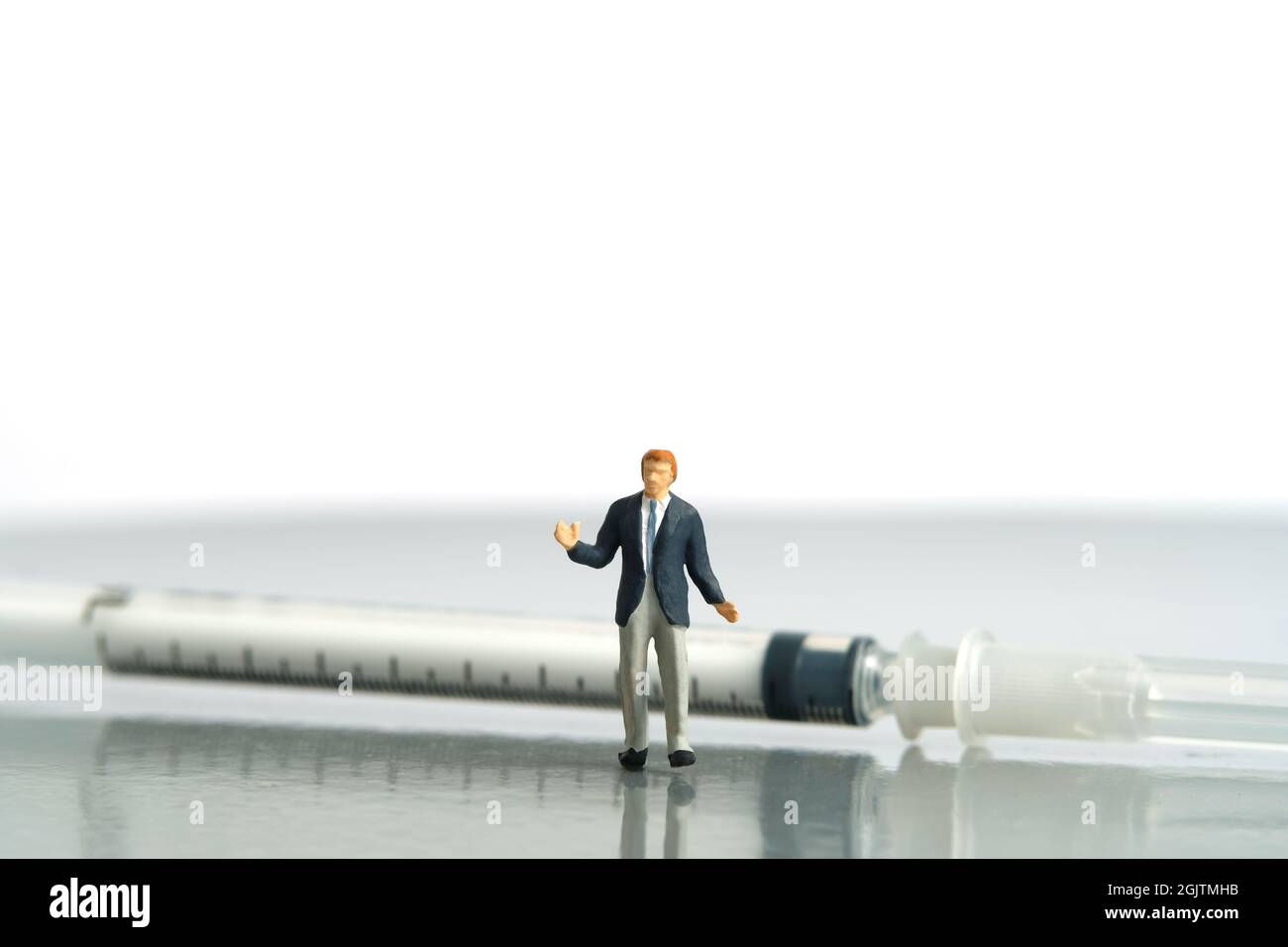 Fotografia di personaggi giocattolo in miniatura. Esitazione sul concetto di vaccinazione. Un uomo d’affari che si sta levando davanti al vaccino a siringa. Isolato su Foto Stock