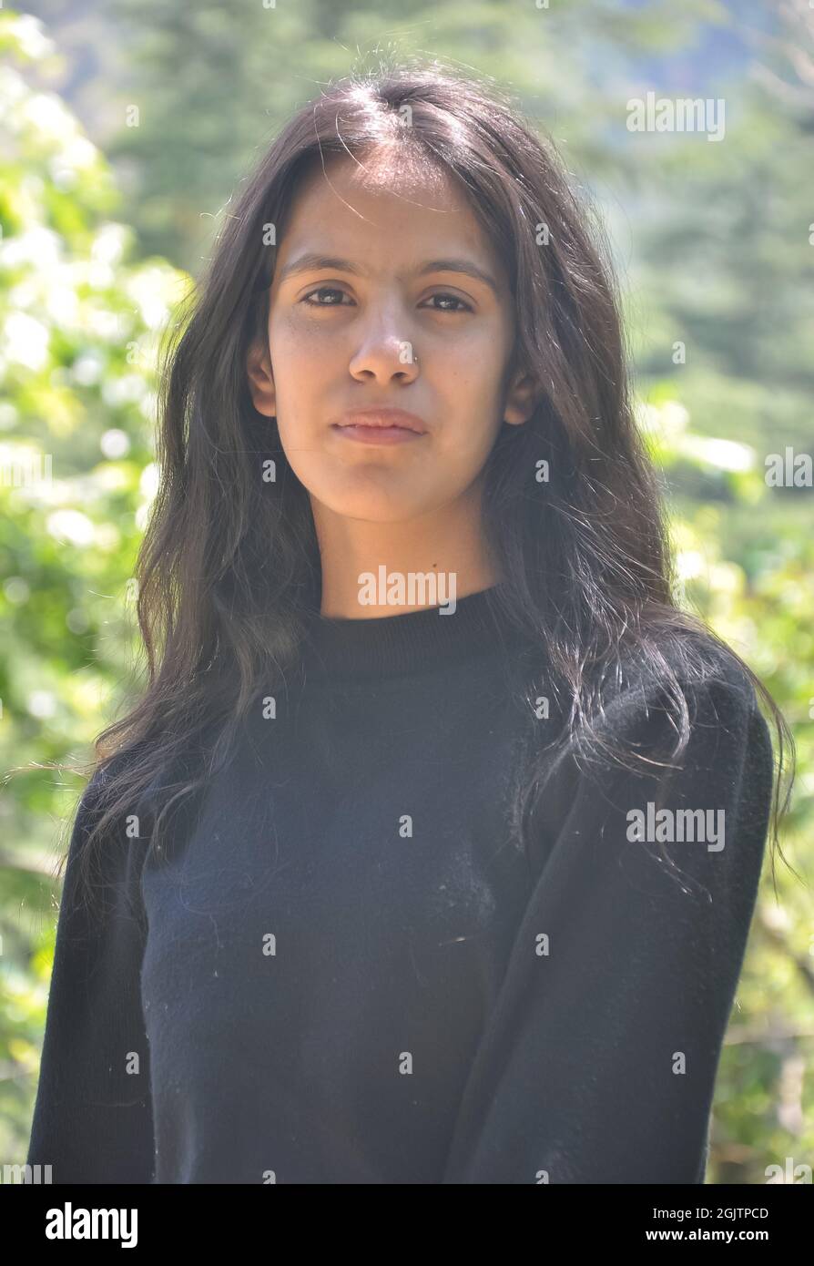 Primo piano di una bella ragazza indiana che indossa una felpa nera, posa all'aperto in natura con guardare la macchina fotografica Foto Stock