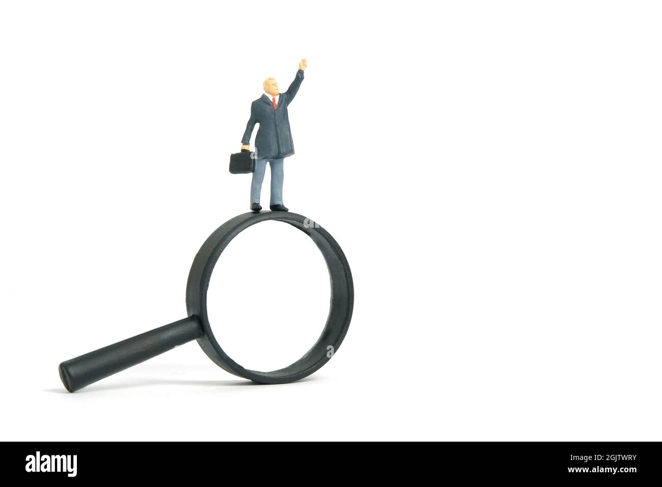 Fotografia di personaggi giocattolo in miniatura. Un uomo d'affari che si trova sopra la lente d'ingrandimento determina per trovare la soluzione. Isolato su sfondo bianco. Immagine Foto Stock