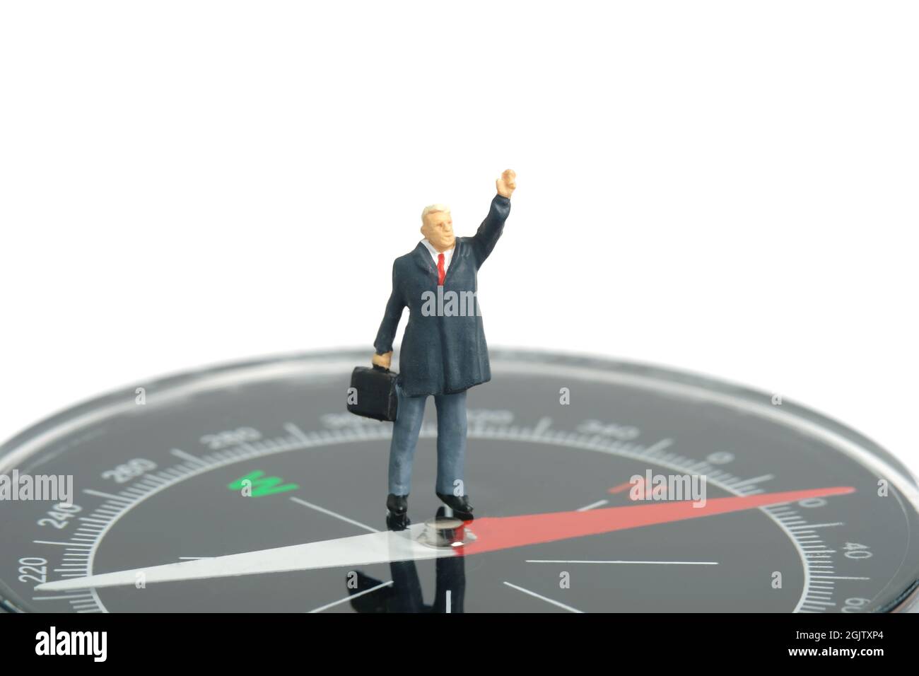 Fotografia di personaggi giocattolo in miniatura. Concetto di direzione aziendale. Un uomo d'affari in piedi sopra una bussola nera mentre alza la mano. Isolato su wh Foto Stock