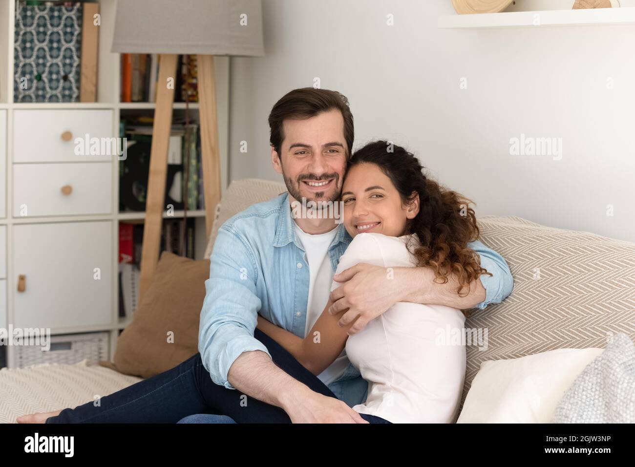 Coppia felice abbracciando sedersi sul divano sorriso guardare la fotocamera Foto Stock