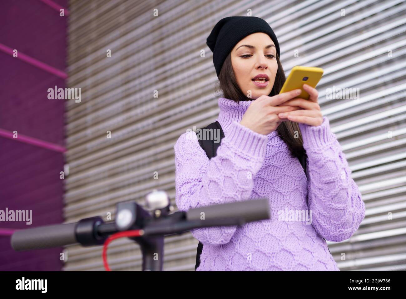 Donna negli anni '20 con scooter elettrico che registra note vocali con uno smartphone all'aperto. Foto Stock