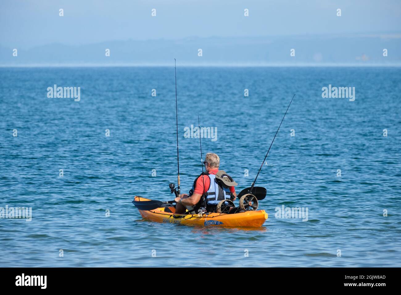 Un pescatore si dirige verso il mare da Broughton Bay, Gower, Galles, ben attrezzata con il suo kayak di mare, canne da pesca in detentore, e giubbotto di salvataggio. Foto Stock