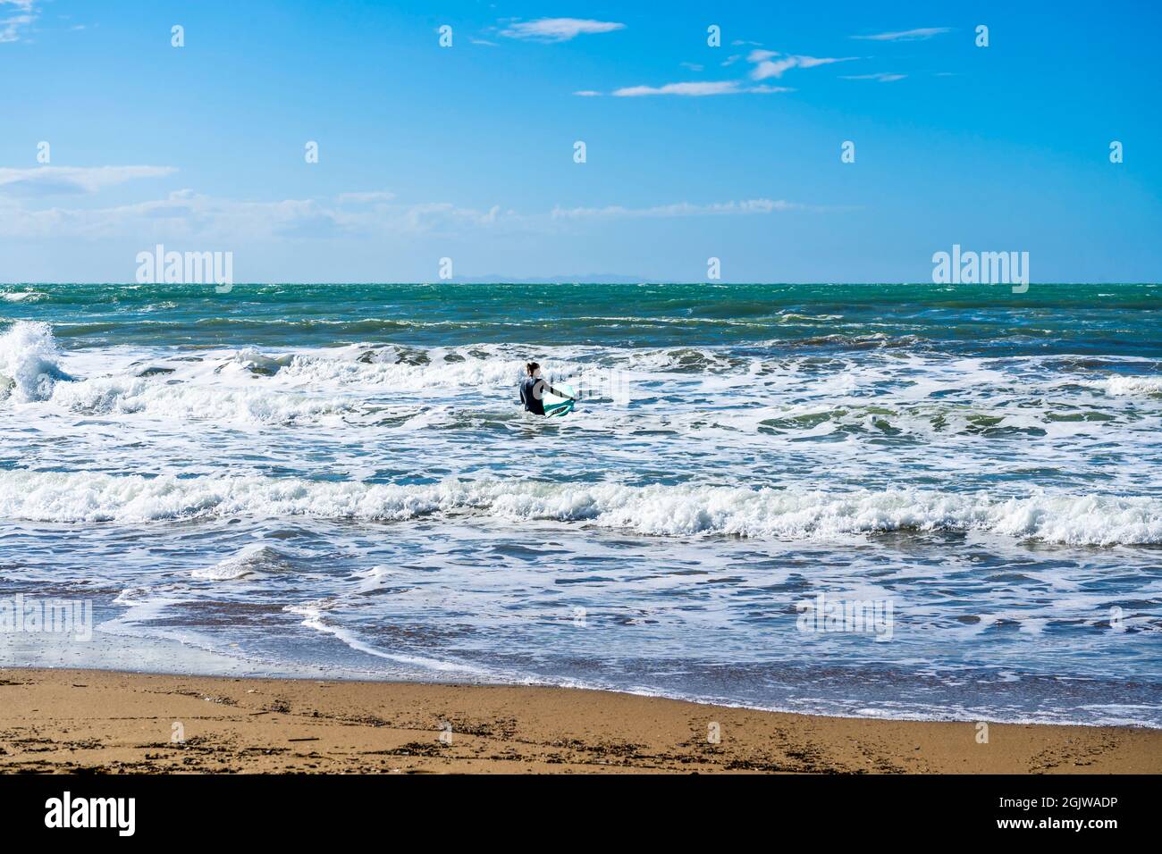 Un surfista che nuota alle onde con la sua tavola da surf, nel golfo di Baratti, Piombino, provincia di Livorno, Italia. Foto Stock