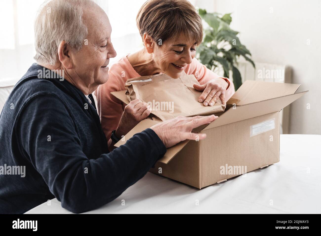 Felice coppia senior disimballaggio consegna scatola di cartone in casa - Focus sul volto donna Foto Stock