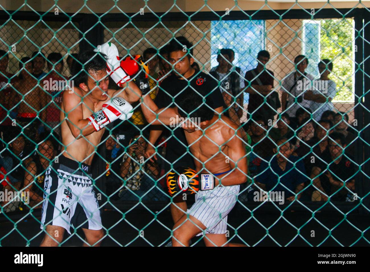 Un arbitro guardò due combattenti MMA (Mixed Martial Arts) che stavano combattendo nel campionato e il pubblico guardò da dietro le gabbie di filo. Foto Stock