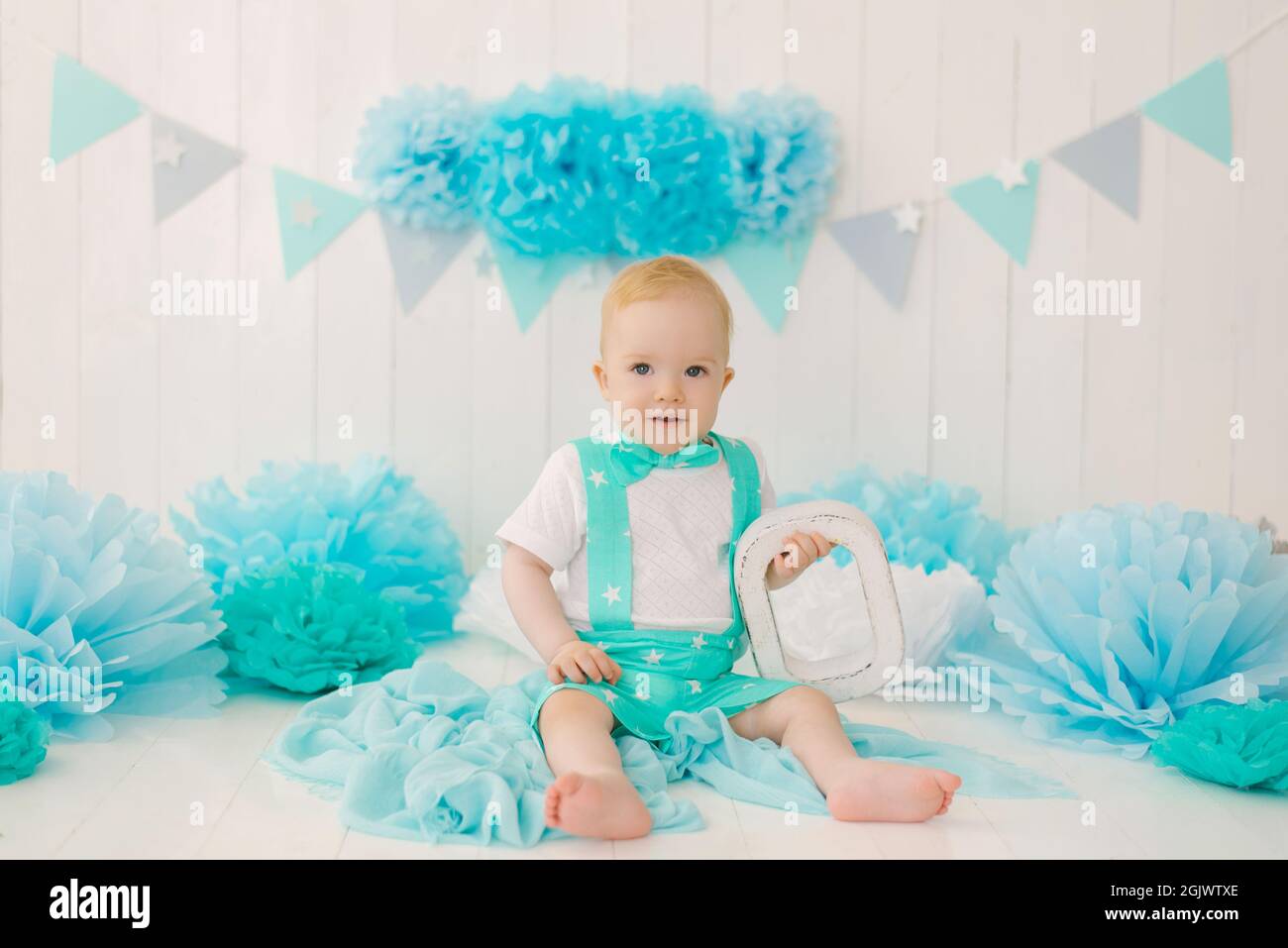 Ragazzo di compleanno ragazzo di 1 anno, babysitter con ghirlande blu e la lettera o in un abito e cravatta ad arco Foto Stock