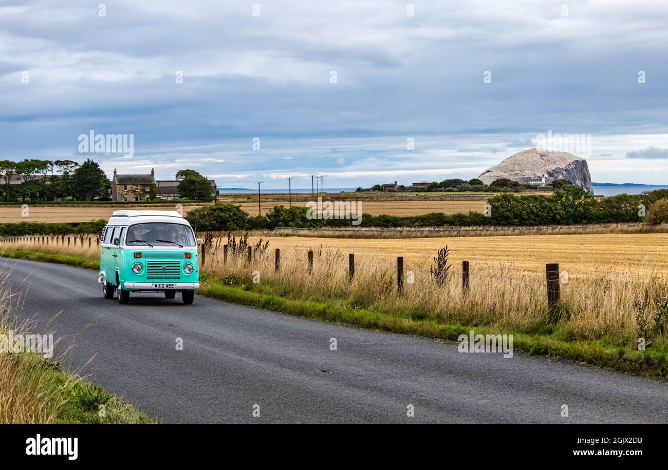 Furgone da camper VW in vecchio stile che guida su una strada di campagna con Bass Rock in lontananza, East Lothian, Scozia, Regno Unito Foto Stock