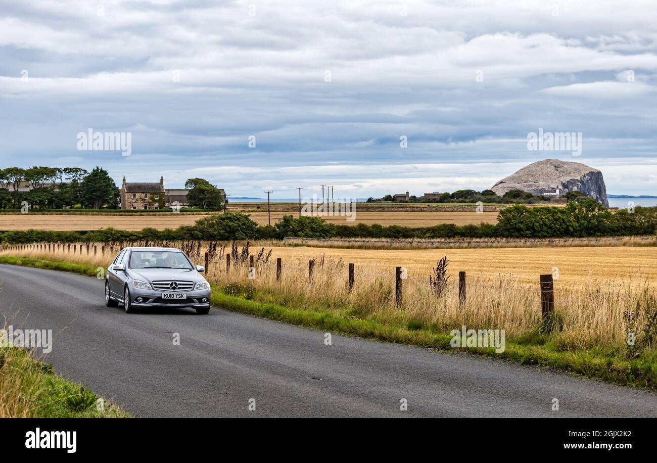 Mercedes auto guida su strada di campagna con Bass Rock Gannet colonia in lontananza, East Lothian, Scozia, Regno Unito Foto Stock