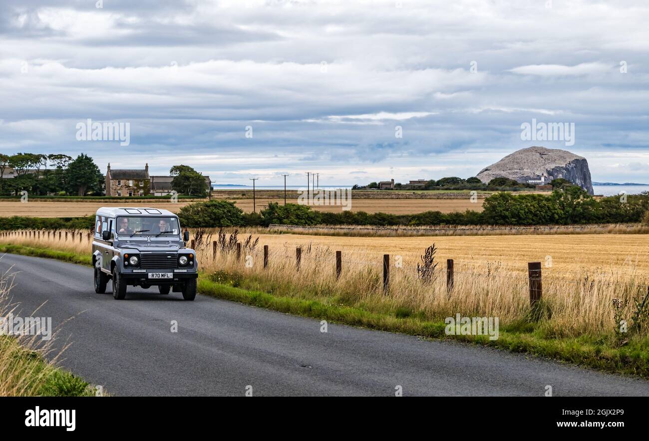 Landrover auto guida su strada di campagna con Bass Rock gannet colonia in lontananza, East Lothian, Scozia, Regno Unito Foto Stock