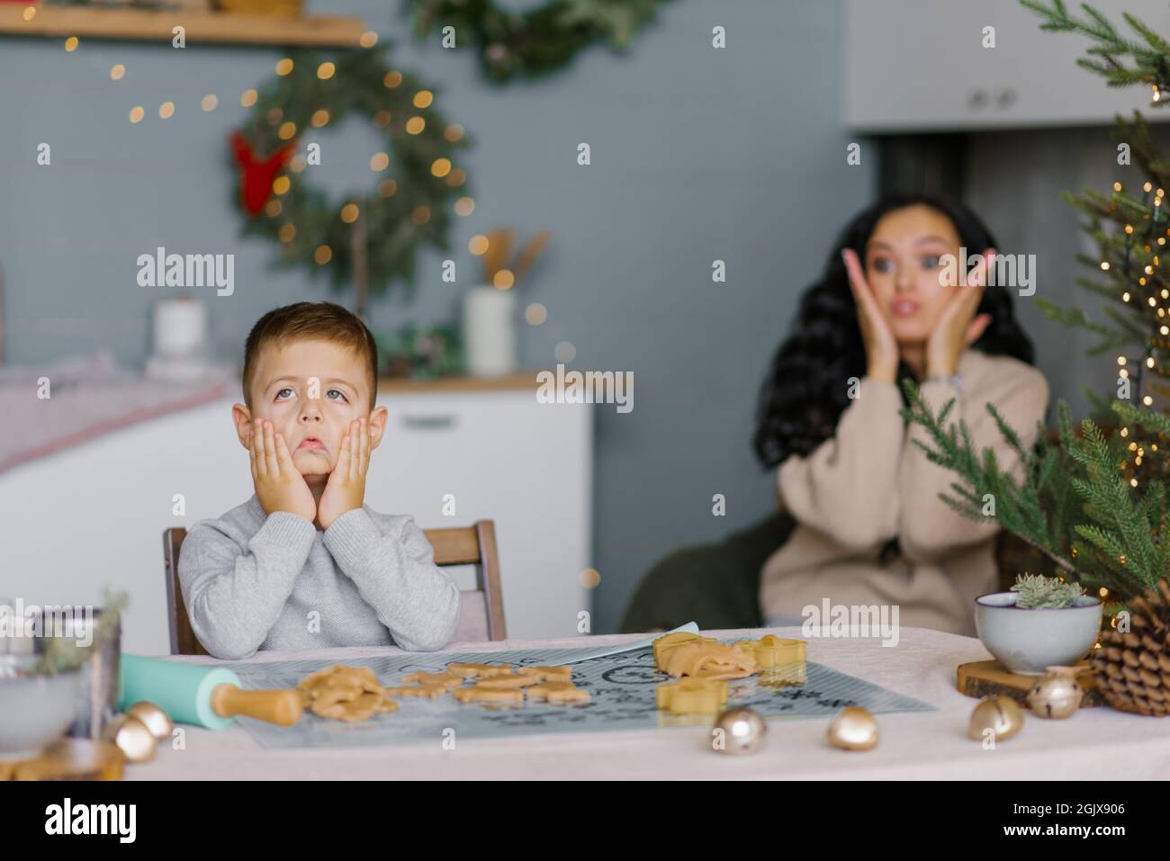 Mamma e figlio fanno i volti e si divertono a preparare i biscotti di Natale in cucina Foto Stock