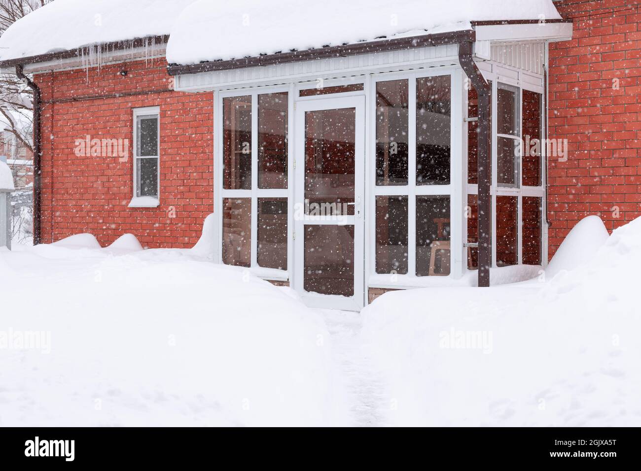 Porta di vetro anteriore di casa di mattoni rossi durante la nevicata pesante Foto Stock