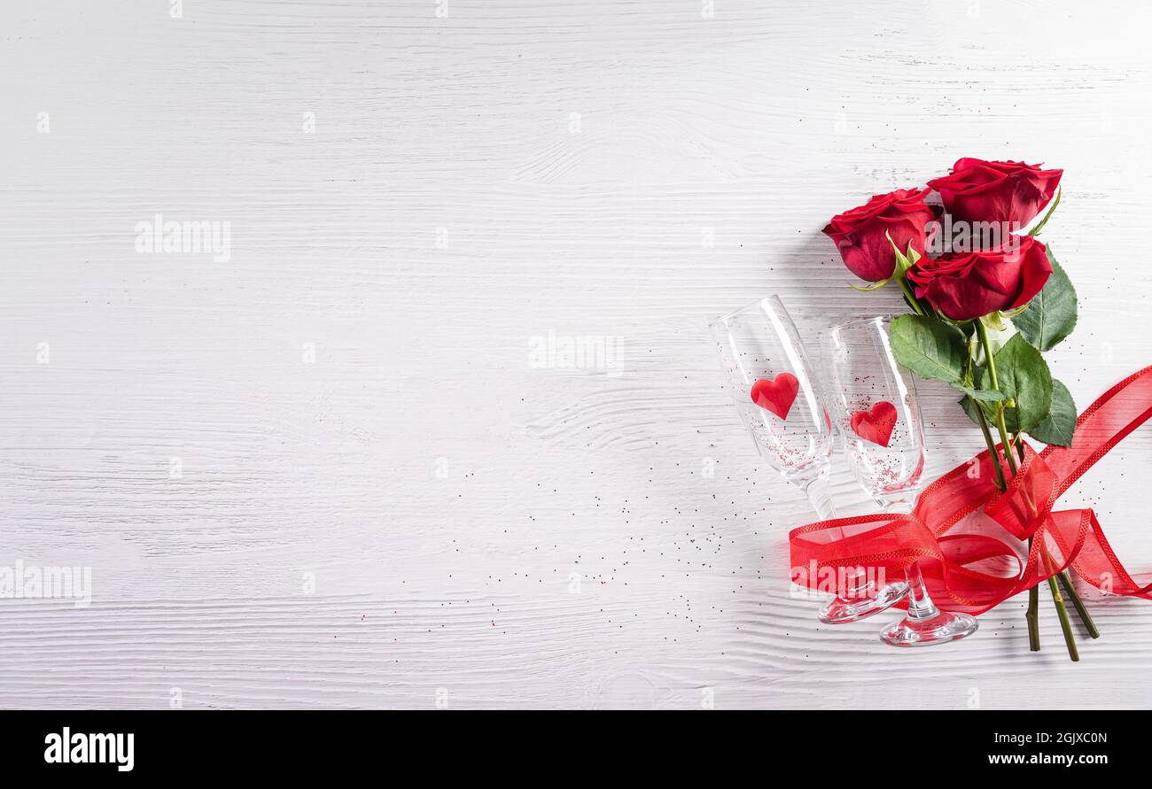 Il concetto Love and San Valentino è realizzato con bicchieri da champagne con cuori rossi e rosa su sfondo bianco in legno. Vista dall'alto con spazio di copia, disposizione piatta. Foto Stock