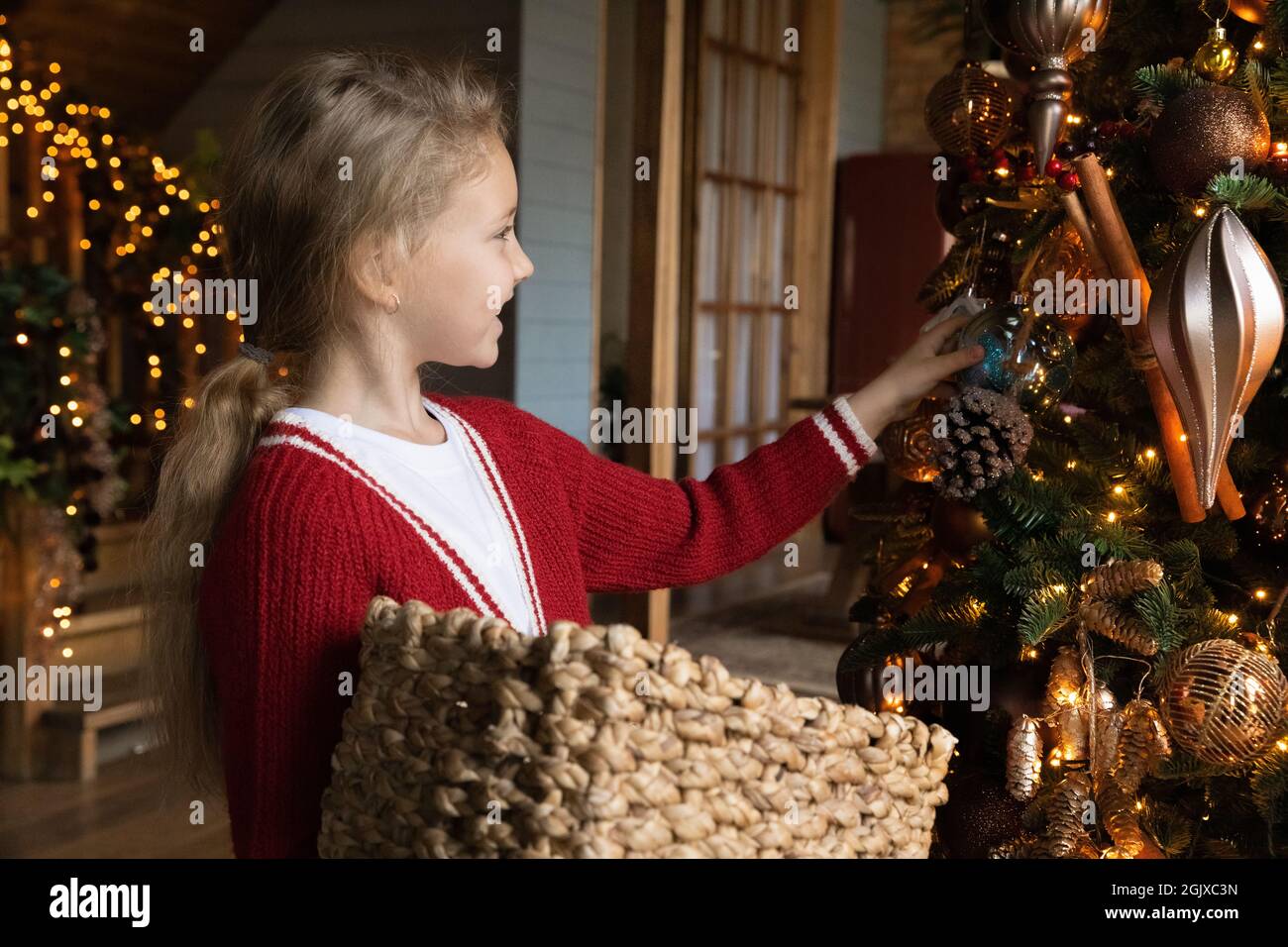 Gioioso carino ragazza carino che tiene il cestino, che decorano l'albero con i baubles. Foto Stock