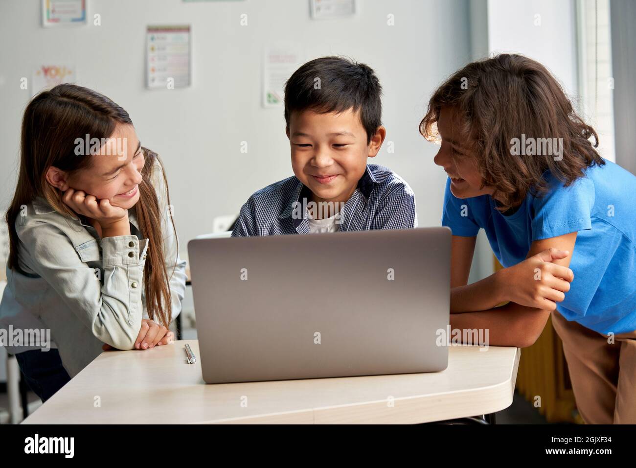 Tre diversi compagni di scuola guardano i video insieme su un notebook in aula. Foto Stock