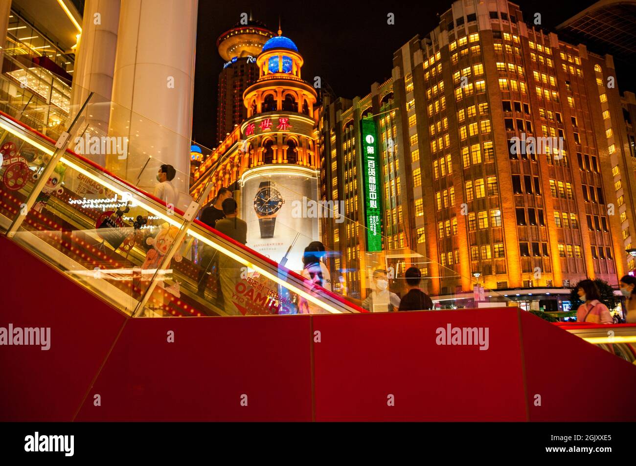 Gli acquirenti salgono la scala mobile presso l'edificio Shimao sulla strada pedonale Nanjing East Road nel centro di Shanghai, Cina, di notte. Foto Stock