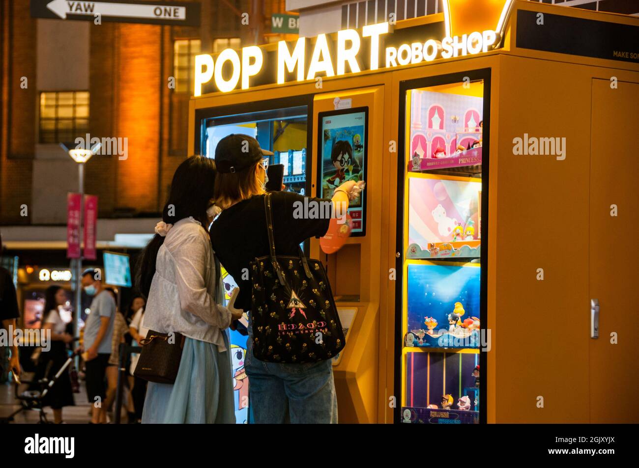 Due giovani donne usano una macchina Pop Mart Robo Shop sotto l'edificio Shimao sulla strada pedonale Nanjing East Road nel centro di Shanghai, in Cina, vicino Foto Stock