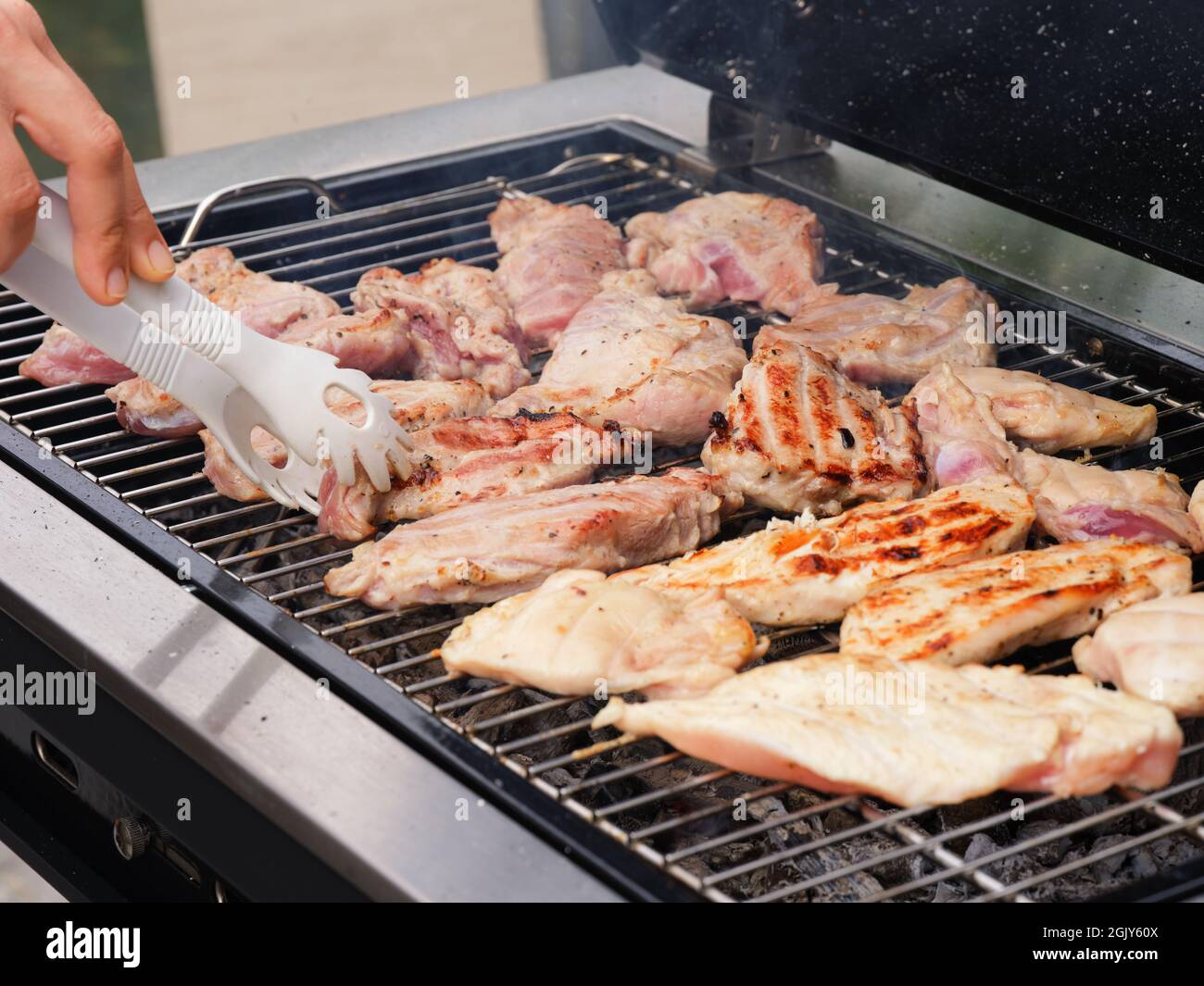 Una donna che cucinava carne su una griglia per barbecue. Primo piano. Foto Stock