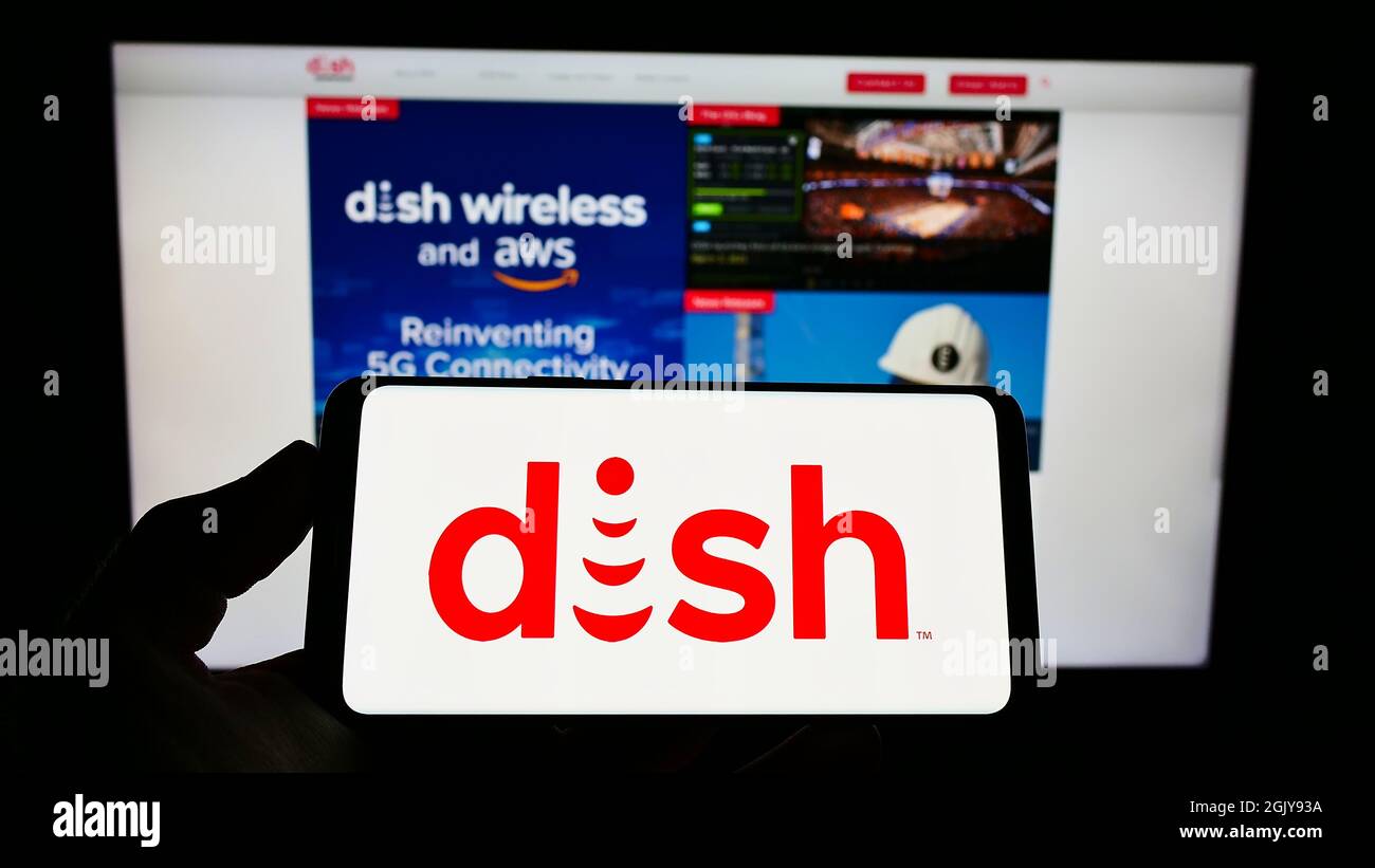 Persona che tiene lo smartphone con il logo della società televisiva statunitense DISH Network Corporation sullo schermo di fronte al sito Web. Mettere a fuoco sul display del telefono. Foto Stock