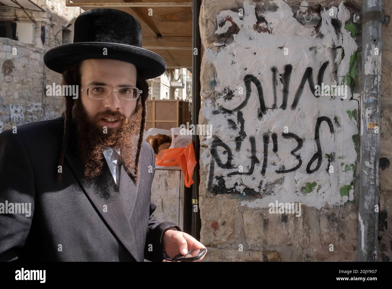 Un ebreo ortodosso cammina accanto a un muro con graffiti contro l'odio sionista spruzzati da ebrei estremisti antisionisti Haredi che recita 'morte ai sionisti' nel quartiere di Mea Shearim, un'enclave ultra-ortodossa a Gerusalemme Ovest Israele Foto Stock