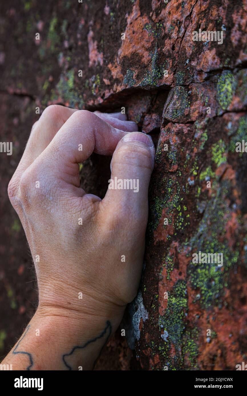 Primo piano di una mano calciosa di un arrampicatore che afferra una piccola presa su una roccia. Foto Stock