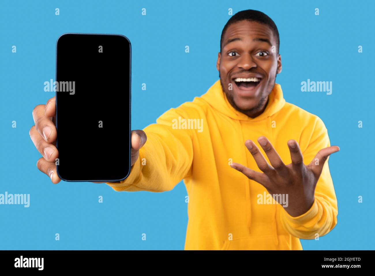 L'uomo afroamericano eccitato mostra lo schermo del telefono su sfondo blu Foto Stock