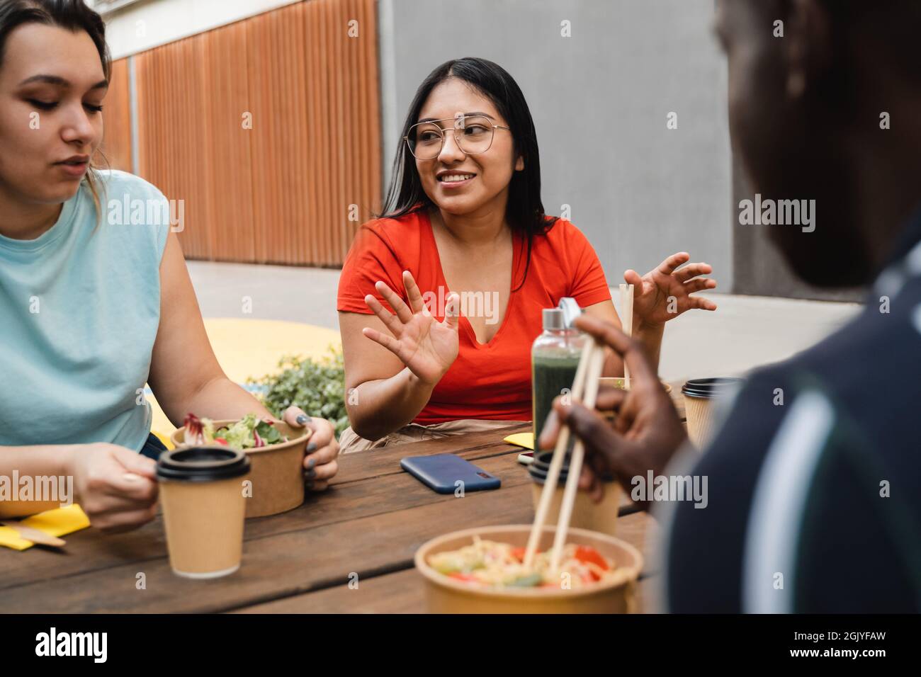 Amici multirazziale divertirsi mangiando portare via il cibo all'aperto in città - Focus on asian ragazza volto Foto Stock
