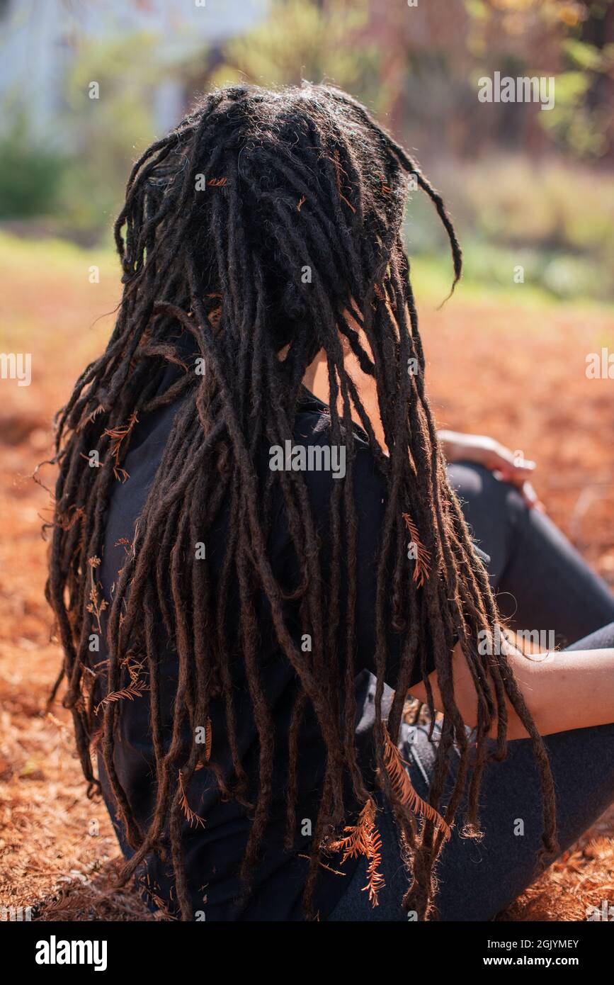 Vista posteriore della donna con i locs seduti all'aperto Foto Stock