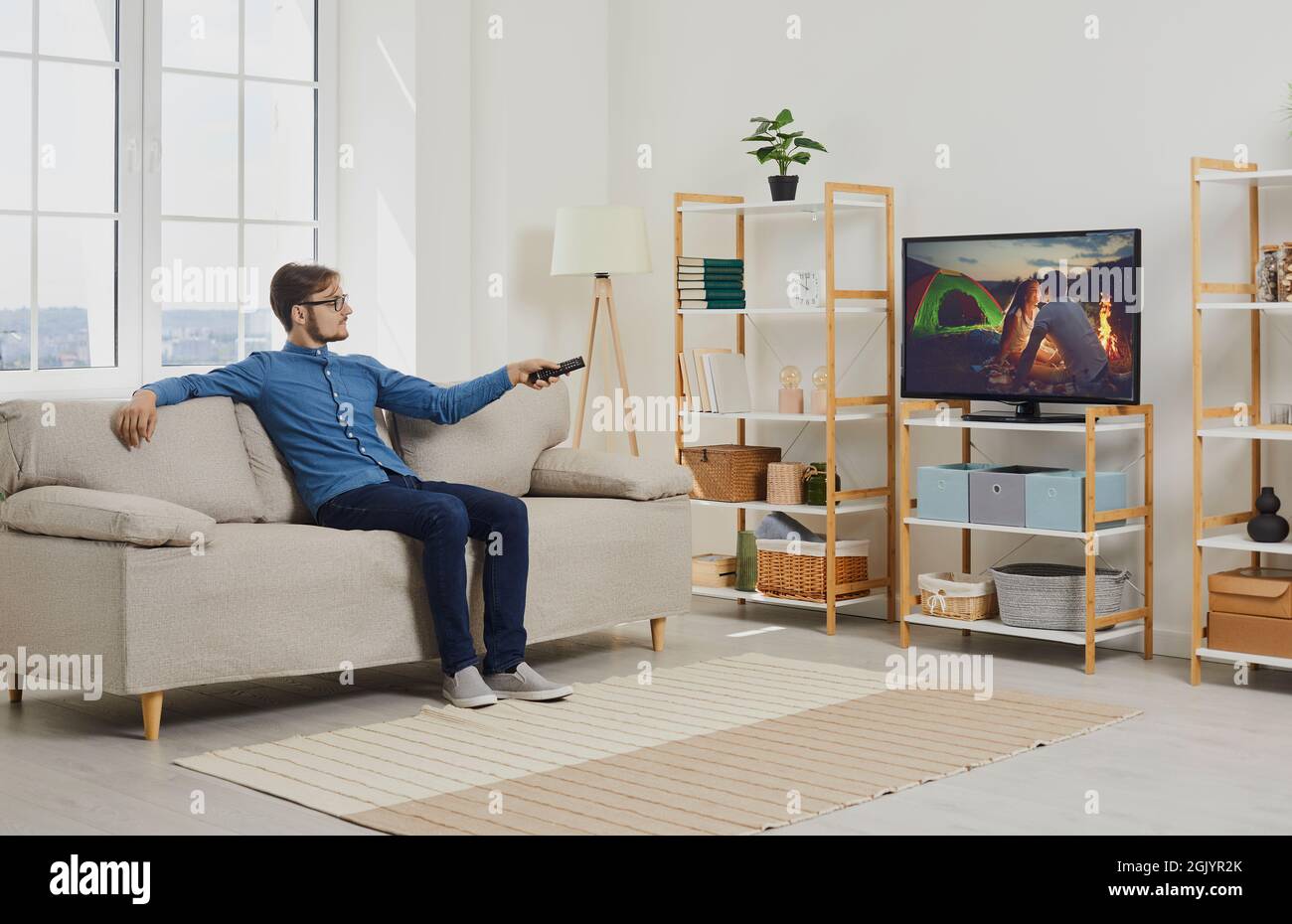 Giovane uomo seduto su un divano nel soggiorno e guardando un film in televisione Foto Stock