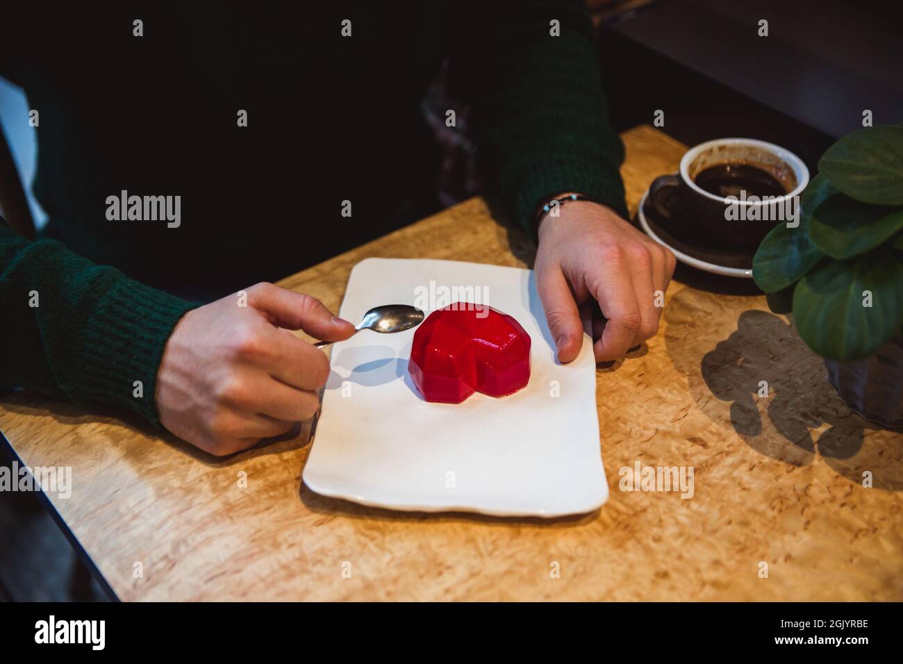 Torta rossa a forma di cuore è sul tavolo. Le mani di Mans con cucchiai si allungano in una torta. San Valentino in caffetteria Foto Stock
