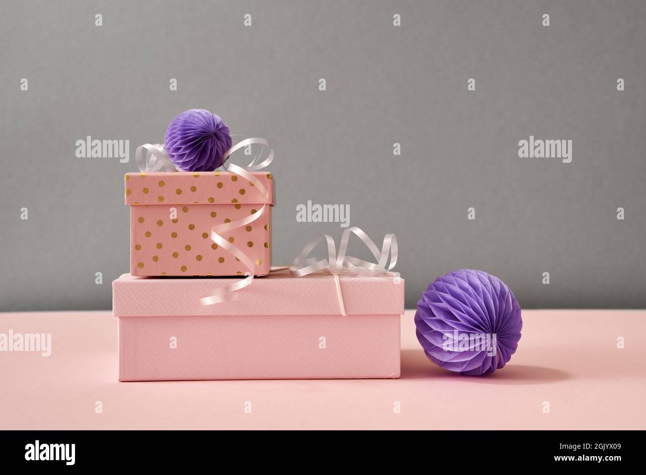 Scatole con regali di Natale e ornamenti in carta viola su sfondo rosa pastello e grigio con spazio copia Foto Stock