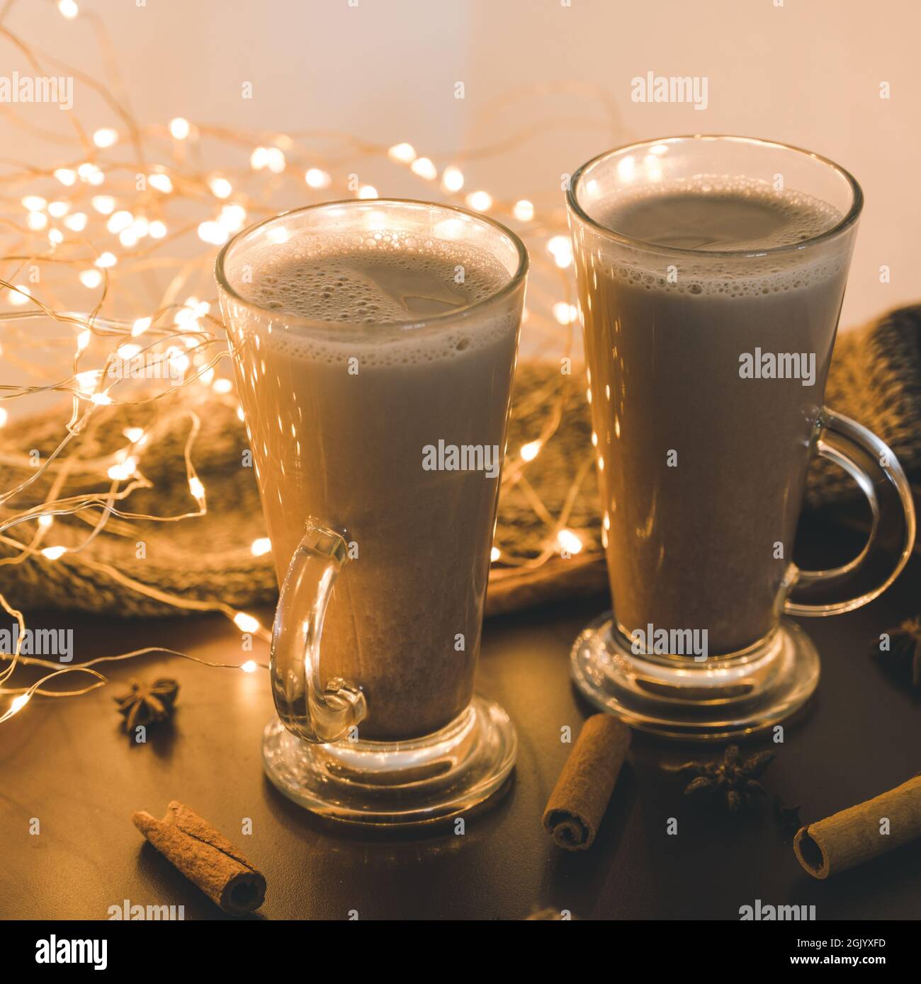 Un paio di bevande calde al cacao in bicchieri su un tavolo marrone. Cioccolata  calda. Sciarpa a maglia. Chiodi di garofano, cannella e anice stellato.  Luci a LED Garland Foto stock -