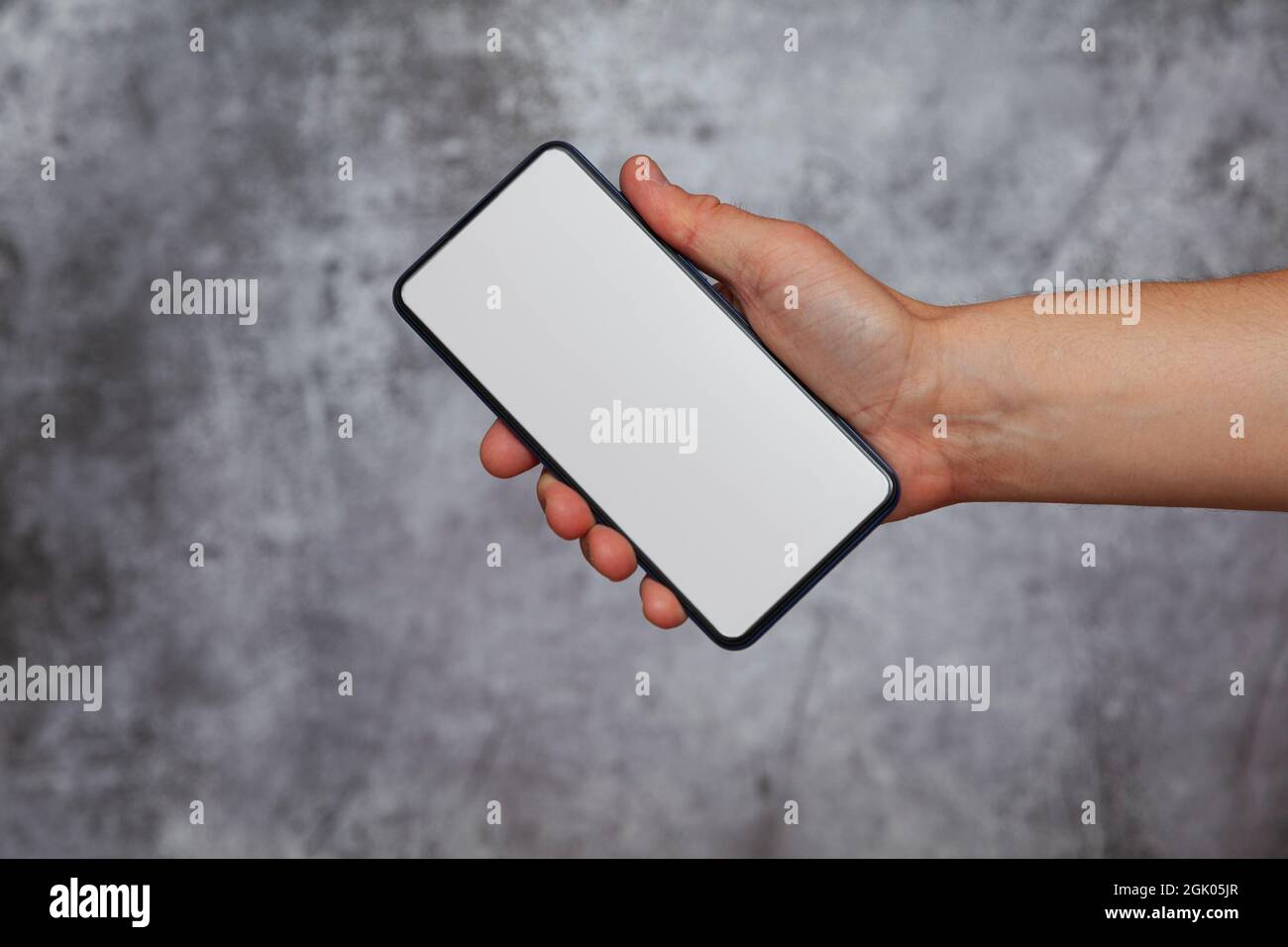 Mano destra di un uomo che tiene uno smartphone con lo schermo acceso e luce bianca su sfondo grigio testurizzato. Foto Stock