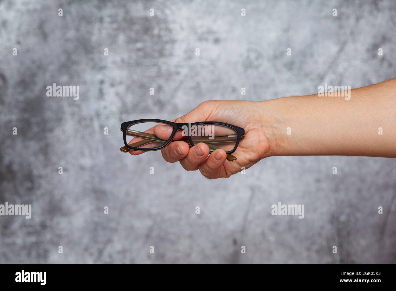 Mano destra di un uomo che tiene un paio di occhiali su uno sfondo grigio testurizzato. Foto Stock