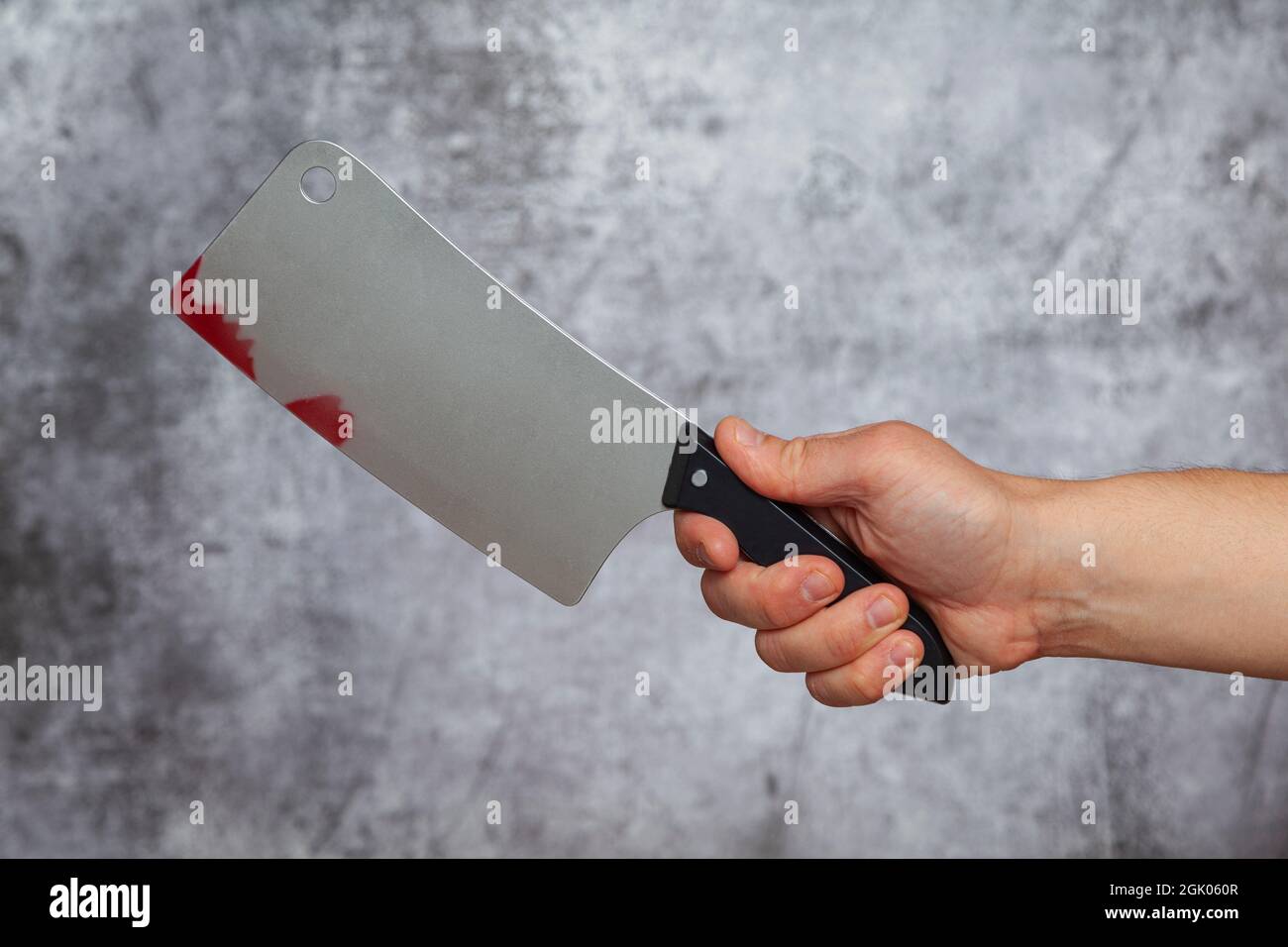 Mano destra di un uomo che tiene un coltello grande macellaio con macchie di sangue su uno sfondo grigio testurizzato. Foto Stock
