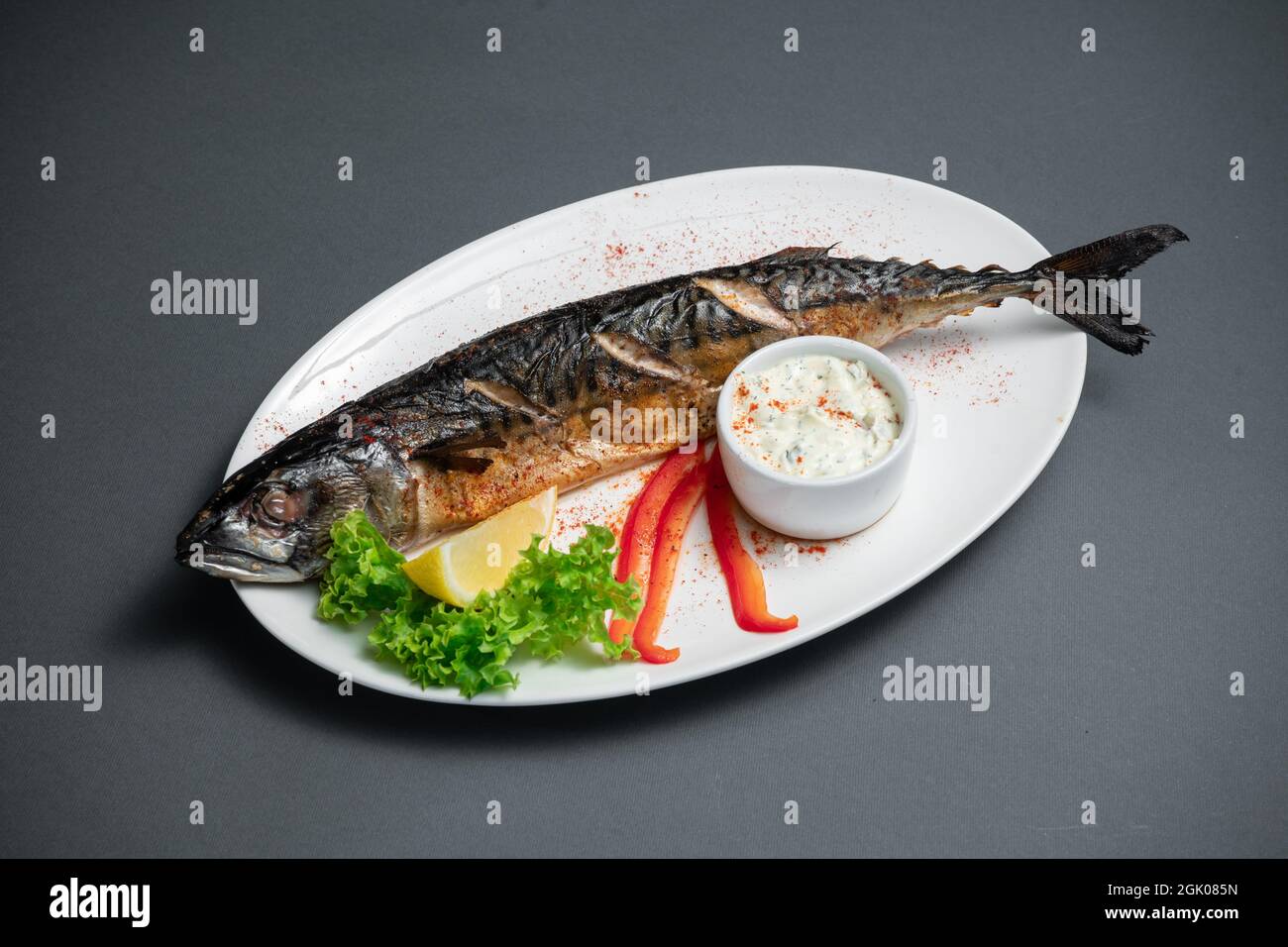 primo piano di sgombro al forno con salsa su piatto bianco su sfondo nero Foto Stock