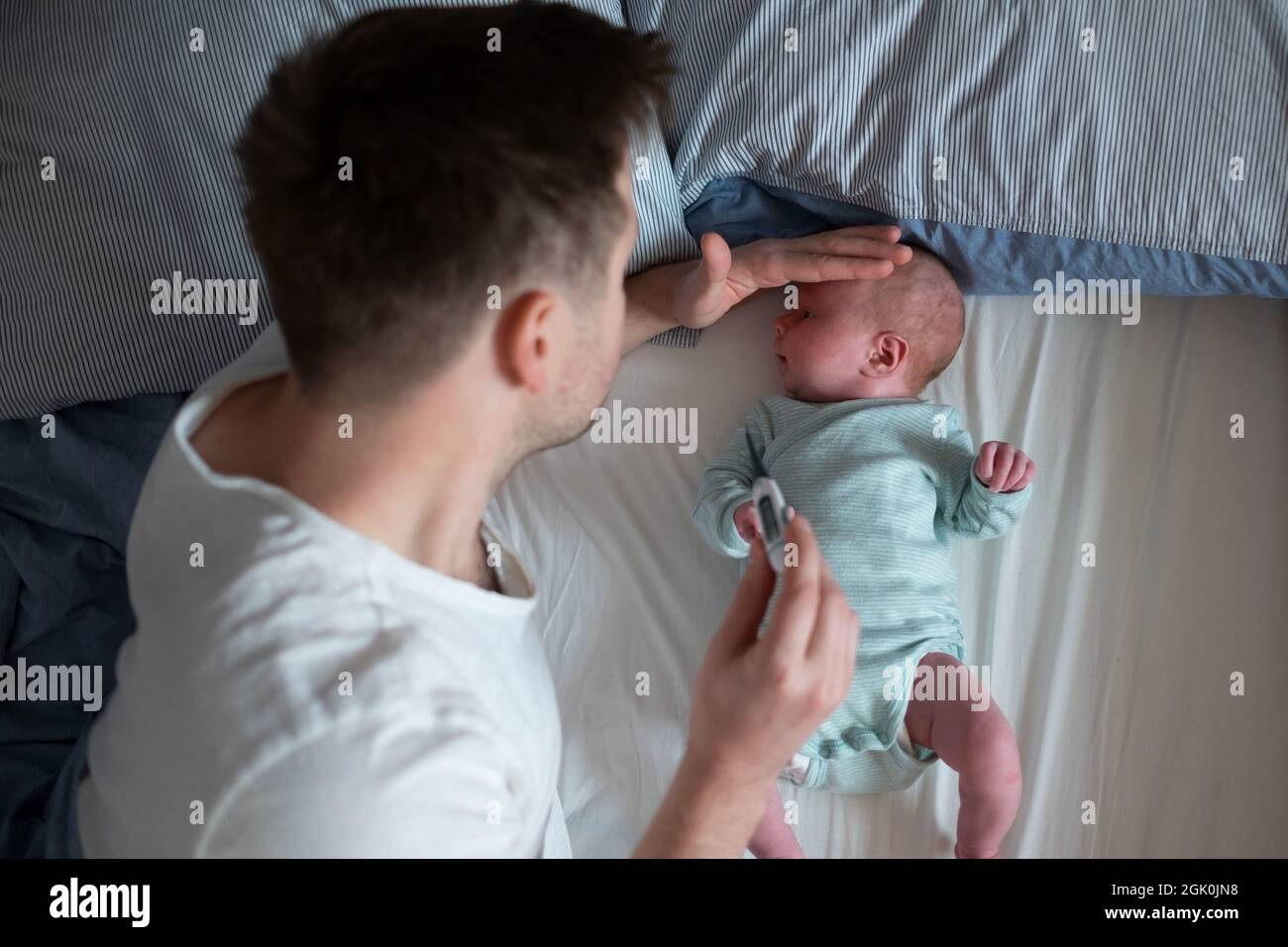 Preoccupato il padre di un'unga che guarda il termometro che tiene il suo neonato nelle mani. Foto Stock
