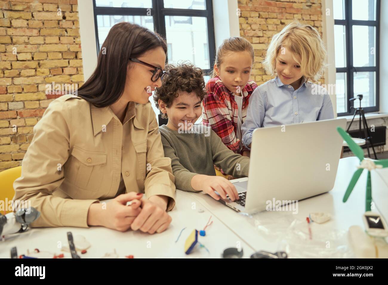 Alfabetizzazione digitale. I bambini intelligenti imparano a programmare utilizzando il computer portatile, seduti al tavolo di un'aula insieme a una giovane insegnante durante la classe STEM Foto Stock