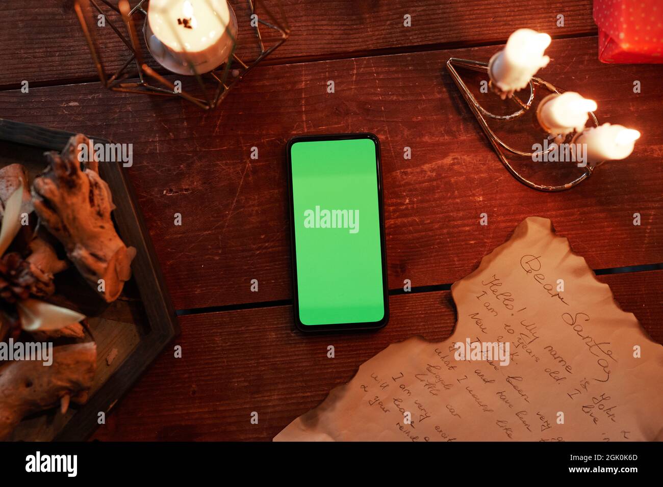 Direttamente sopra la vista dello smartphone con schermo verde, candele e lettera bruciate su un tavolo di legno Foto Stock