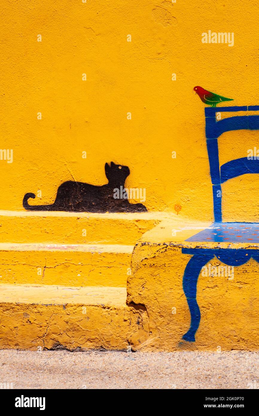 Famosa illustrazione sul muro di Linosa di un gatto che guarda un uccello seduto su una sedia, l'isola di Pelagie. Sicilia Foto Stock