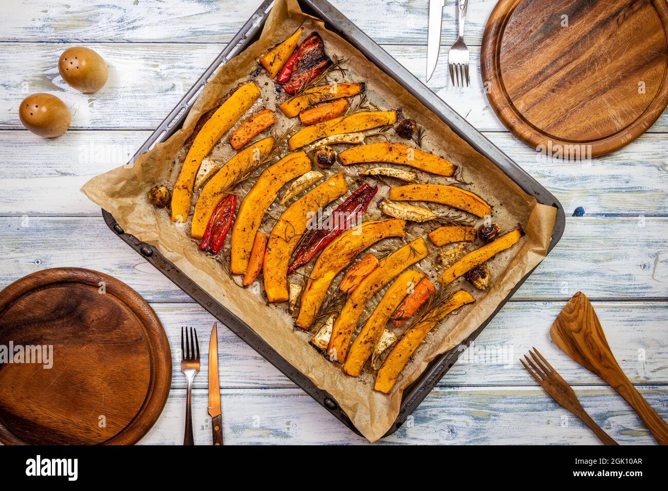 Posizionare l'ambiente con piatti di legno, posate rustiche e zucca cotta nel vassoio da forno sul tavolo da pranzo. Cibo vegetariano sano cucinato per il gelo di ringraziamento Foto Stock