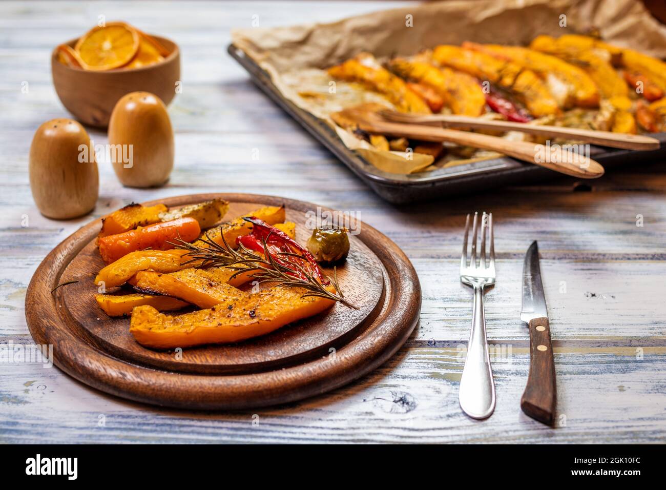 Serve zucca e verdure cotte su piatto di legno. Verdure arrosto come pranzo di ringraziamento autunno. Impostare il tavolo con posate rustiche Foto Stock