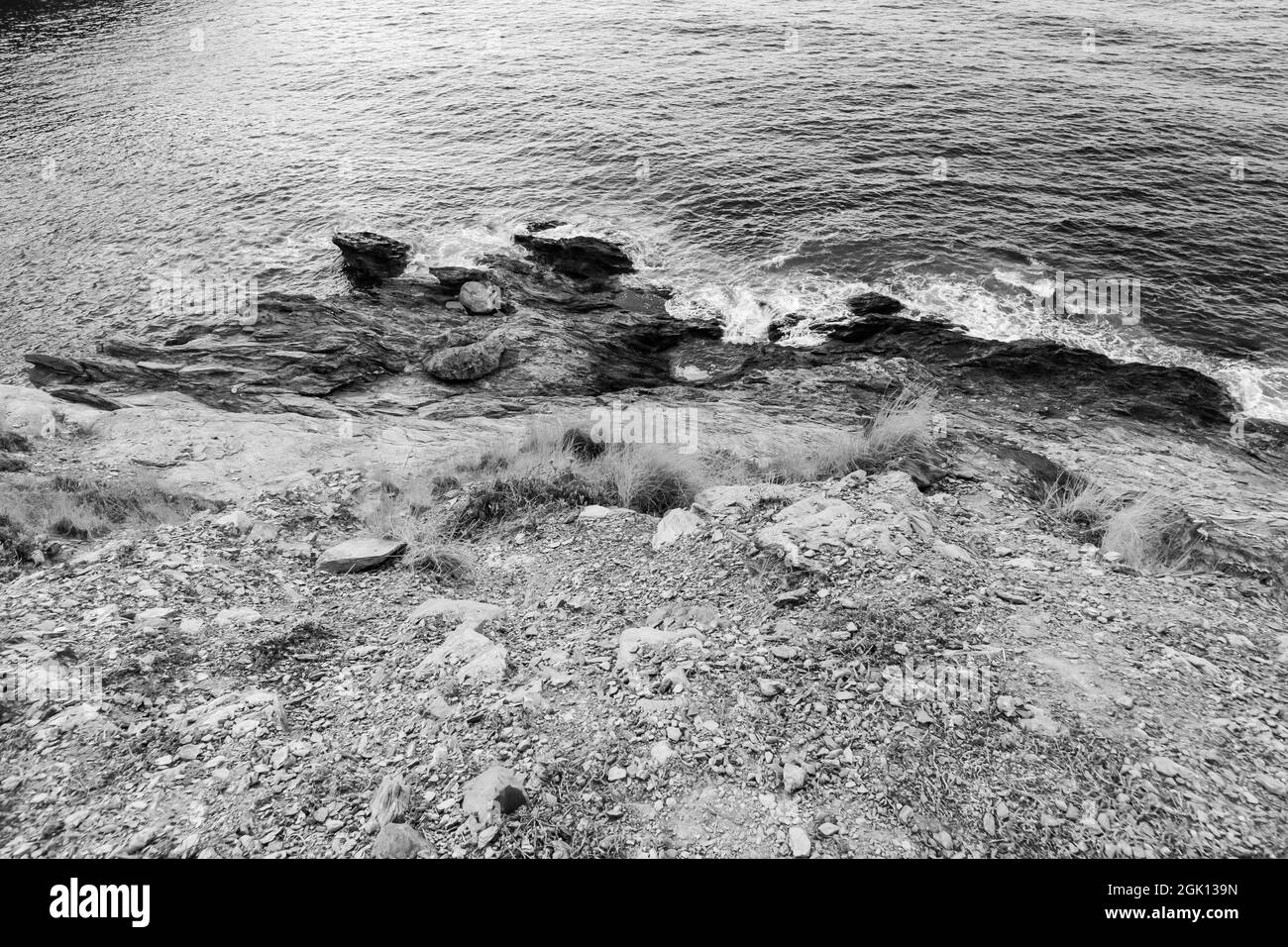 Una foto in scala di grigi dalla cima di una scogliera rocciosa su acqua blu in una giornata di sole Foto Stock